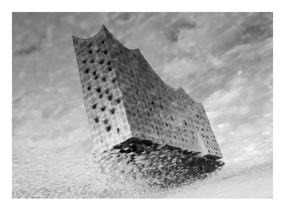 Black and white reflection of the Elbphilharmonie Hamburg concert hall mirrored in a puddle on the ground.