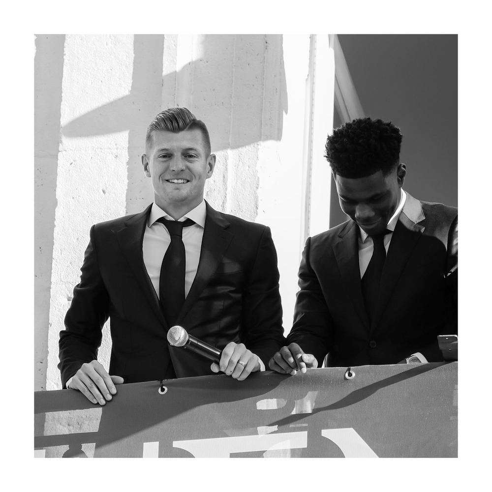 Two men in black suits and ties smile on a balcony in a black and white photo.