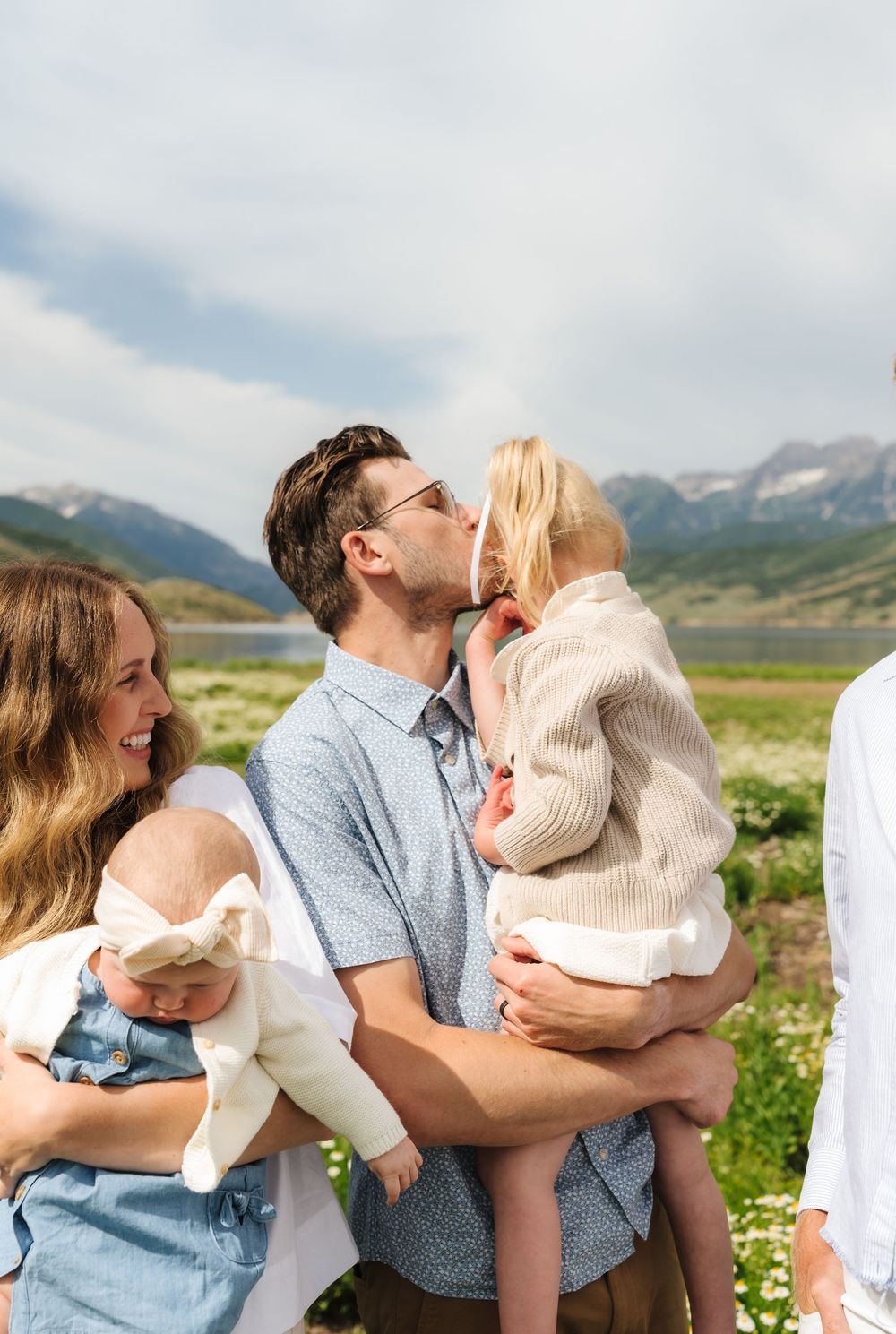 A happy family with two young children shares a tender moment in a scenic mountain meadow on a sunny day.