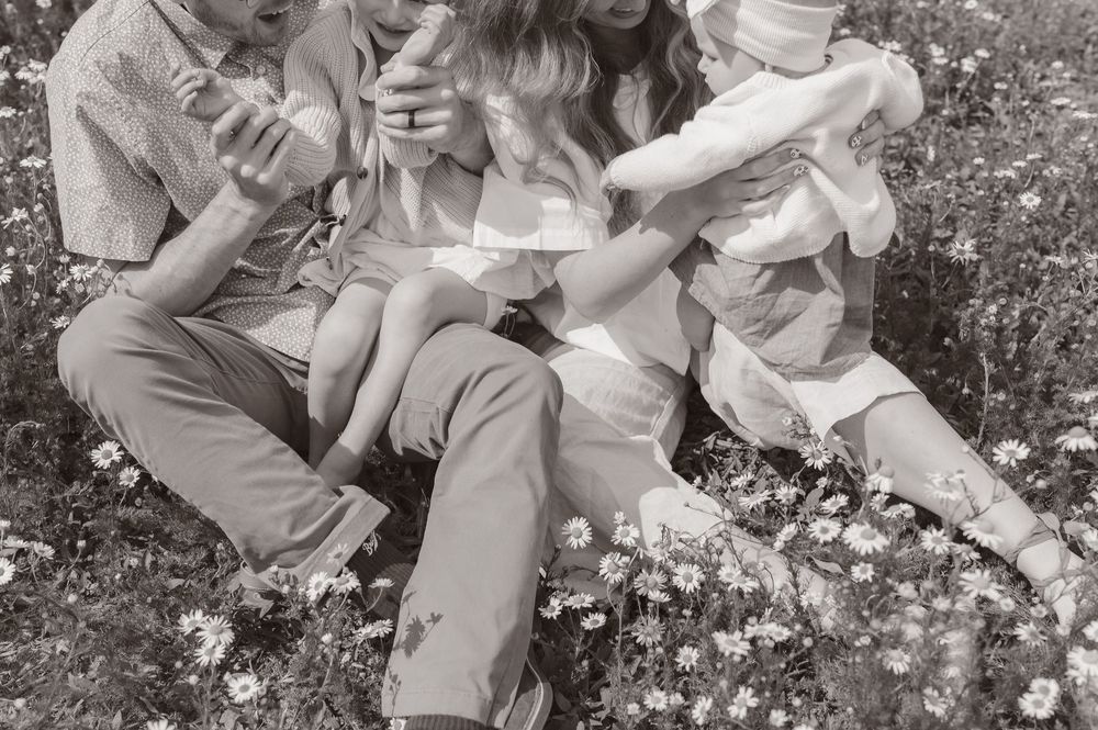 Black and white photo of a family sitting together in a wildflower meadow, sharing a joyful moment outdoors.