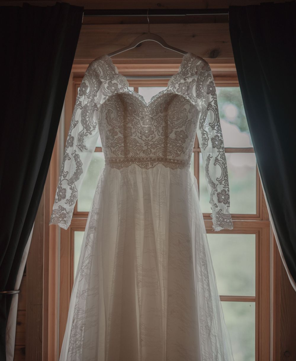 Elegant lace long-sleeve wedding dress hanging in a sunlit wooden window frame.