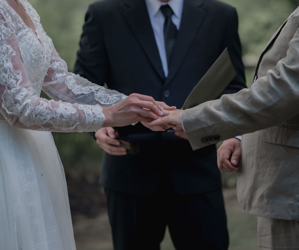 Bride and groom exchange rings during an outdoor wedding ceremony with officiant.