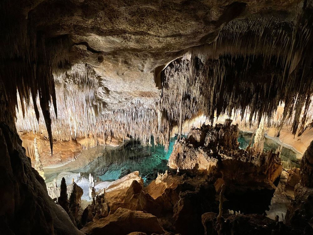 Stunning cave interior with stalactites hanging from ceiling above a turquoise underground lake in a limestone cavern.