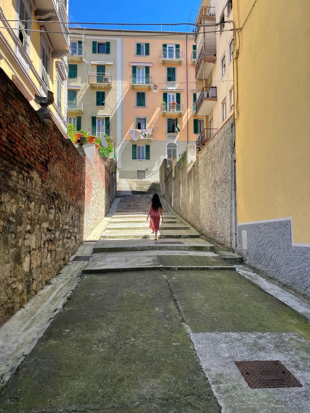 A woman in a red dress walks up stone steps in a narrow alley between colorful Italian buildings.
