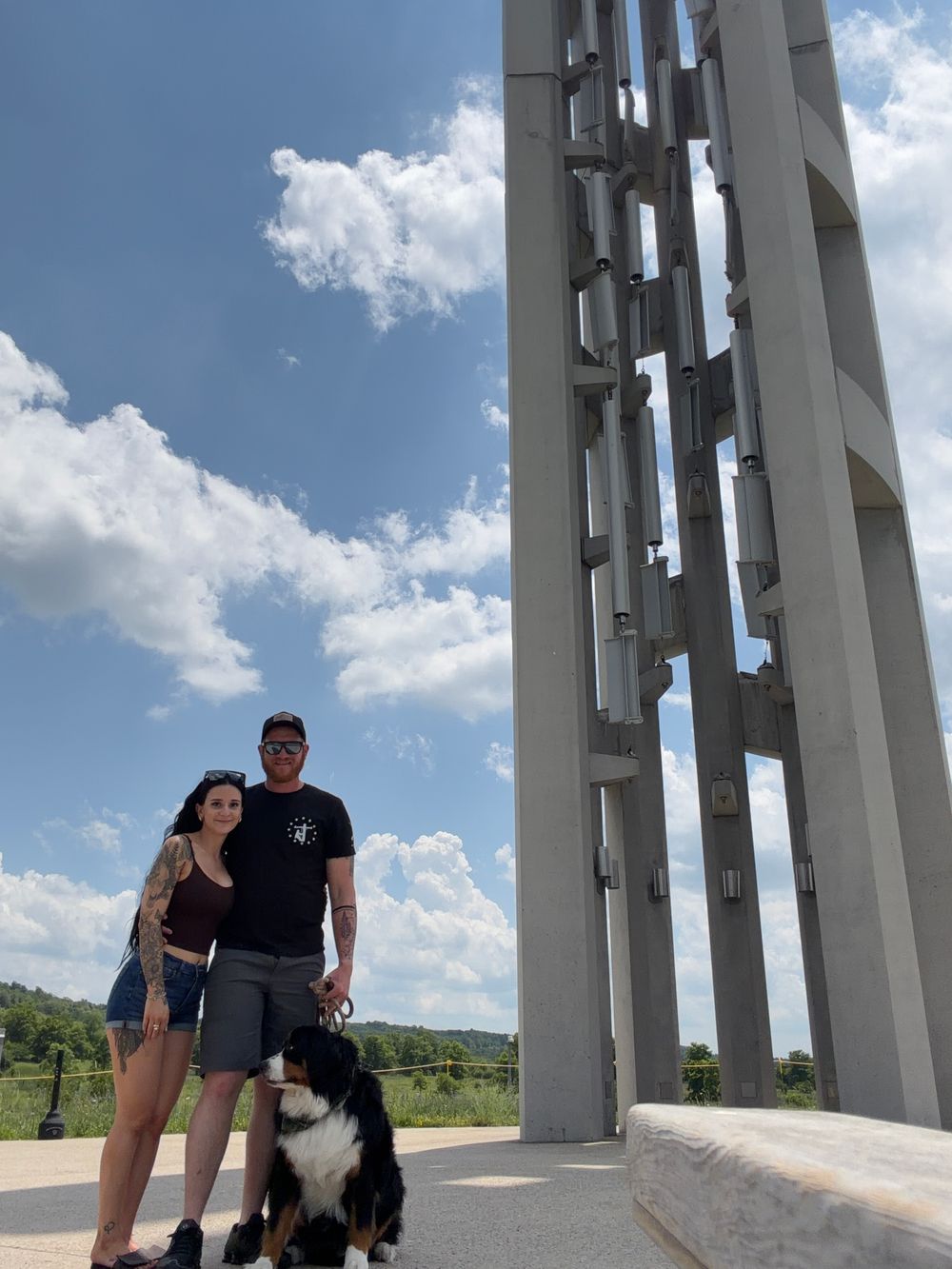 Couple with Bernese Mountain Dog standing at Flight 93 National Memorial tower on a sunny day.