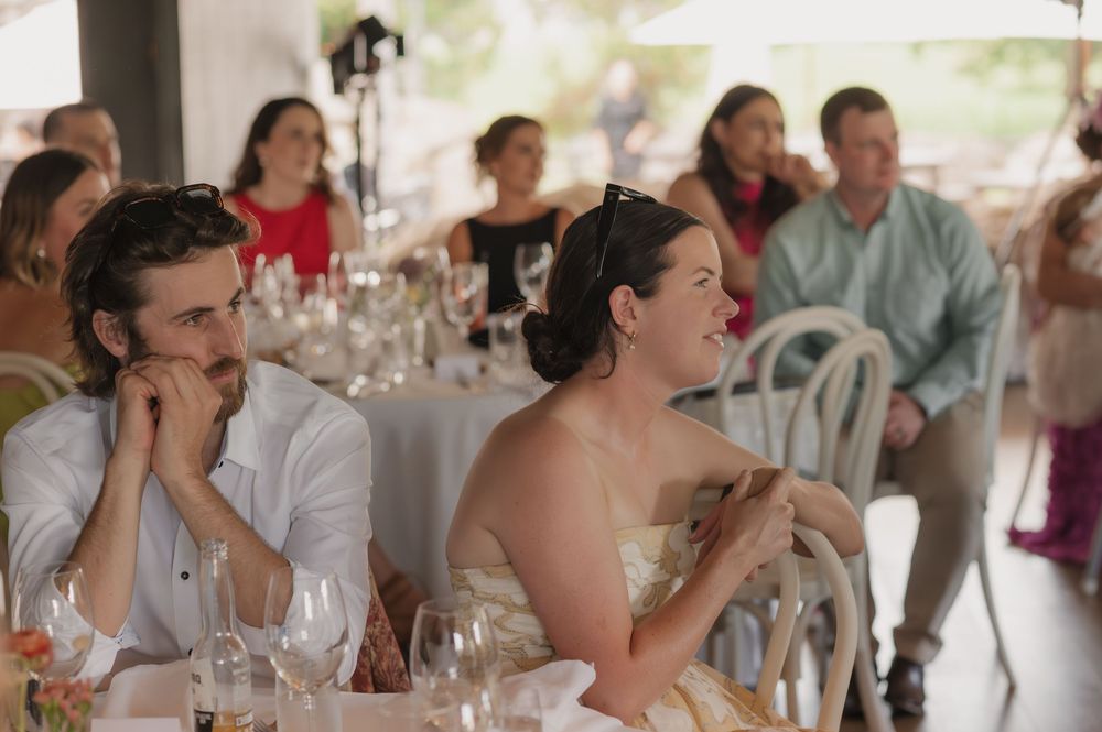 Guests laughing and enjoying conversation at a wedding reception dinner table with wine glasses.