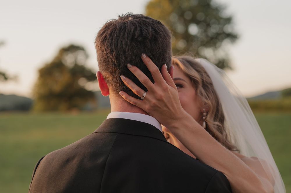 Bride and groom share a romantic kiss outdoors at golden hour during their wedding ceremony.
