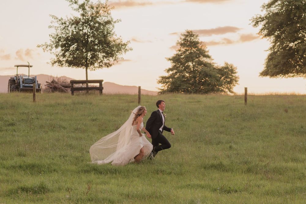 Bride and groom running through a green field at golden hour sunset on their wedding day.