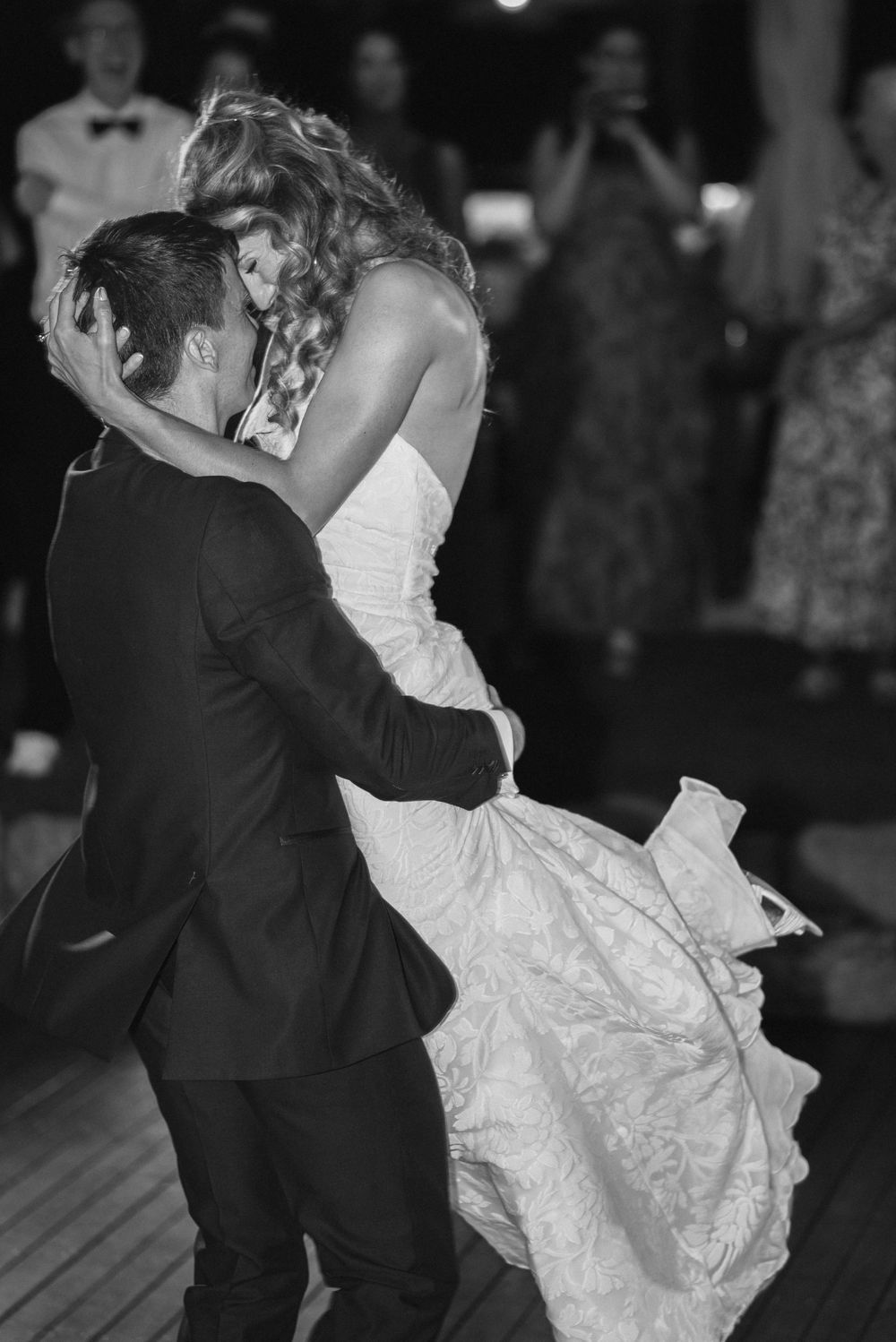 Black and white photo of bride and groom sharing first dance, embracing romantically at wedding reception.