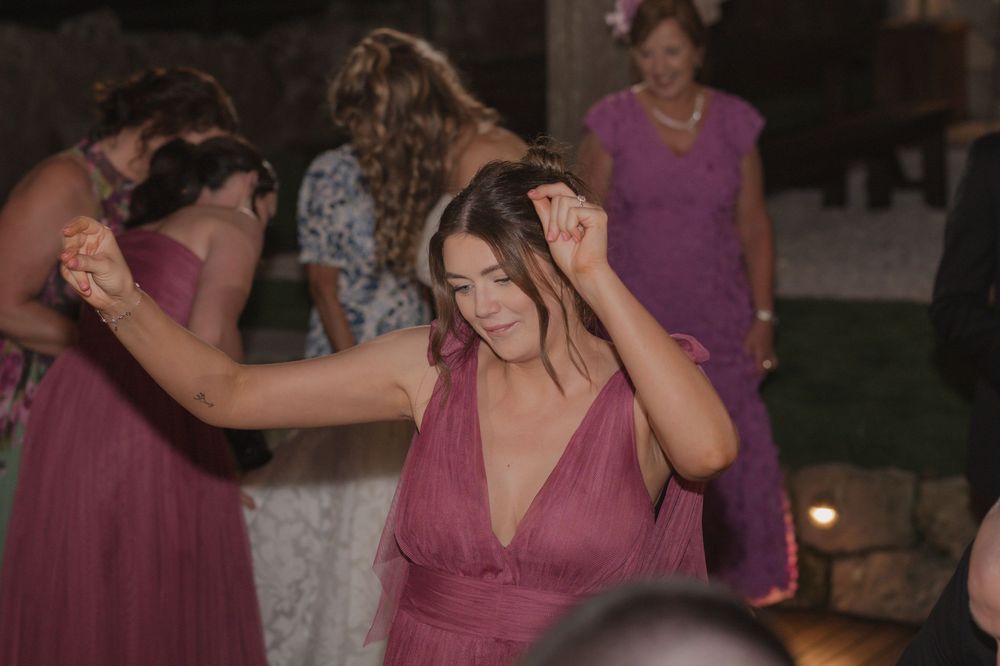 Bridesmaids in dusty rose gowns dancing joyfully at an outdoor wedding reception at night.