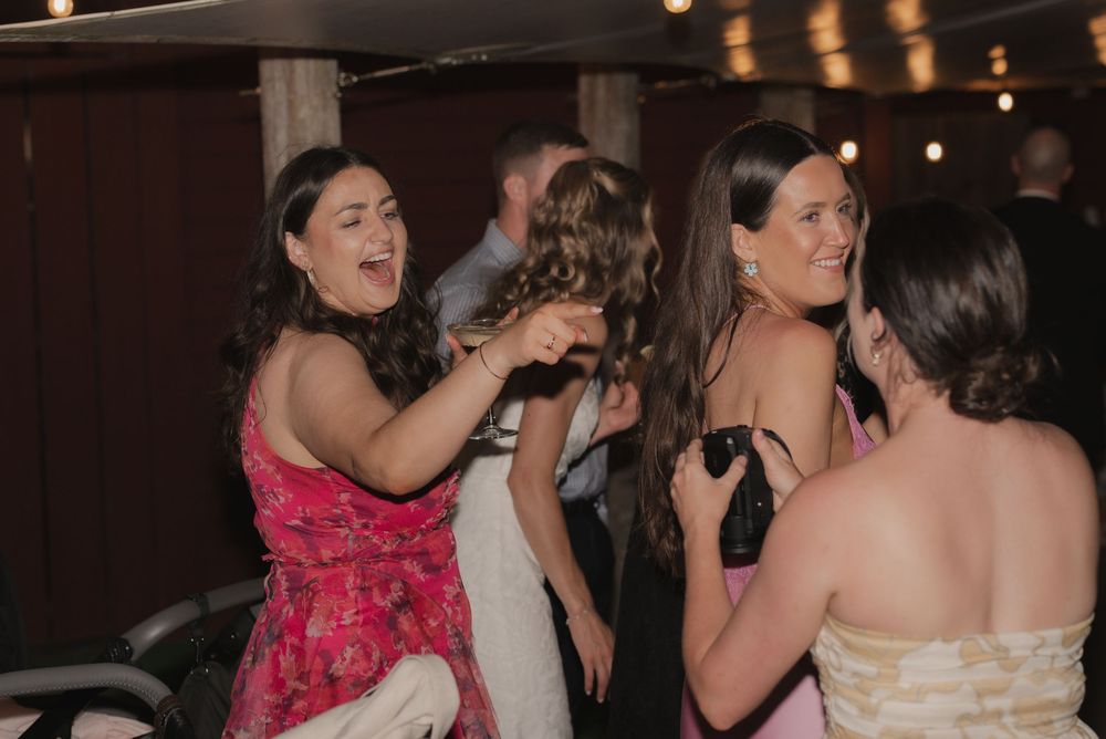 Guests laugh and dance together at a lively wedding reception party indoors.