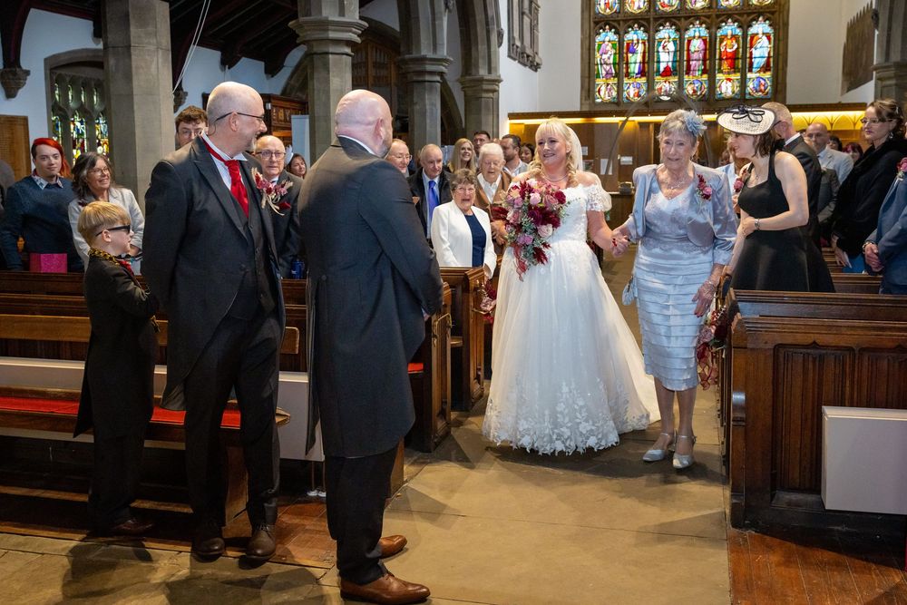 Bride in white gown walks down church aisle with guests watching during a traditional wedding ceremony.