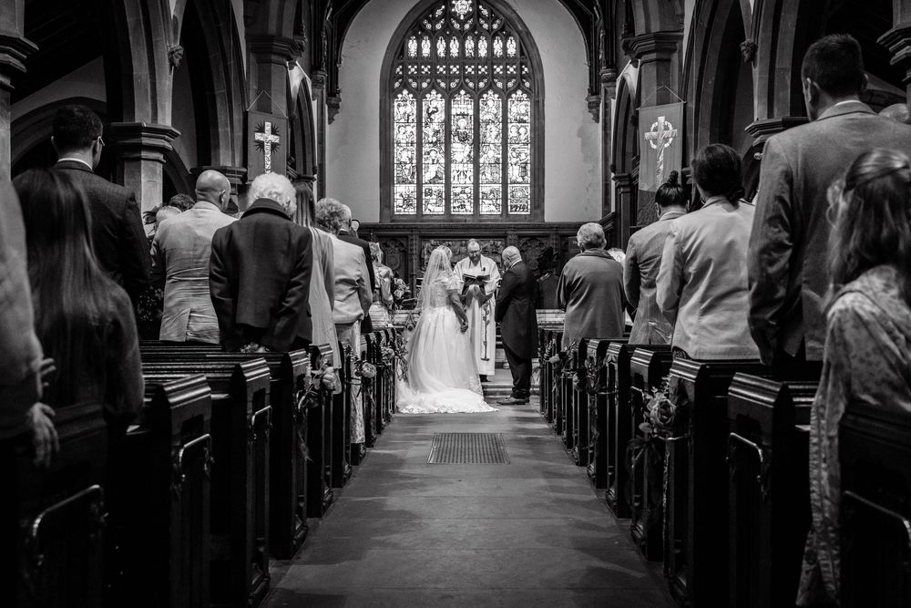 Black and white photo of a church wedding ceremony with guests seated in pews as bride and groom stand at the altar.