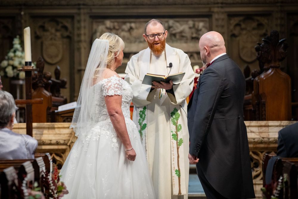 Bride and groom exchange vows before a red-bearded officiant in a grand church during a traditional wedding ceremony.