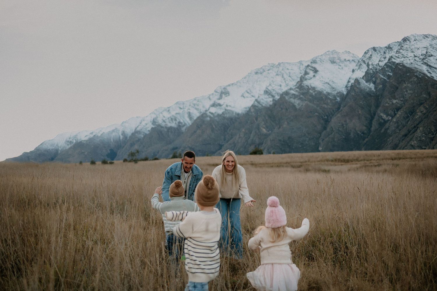 Family of five posing on a rocky lakeside beach with mountains and calm water in the background.