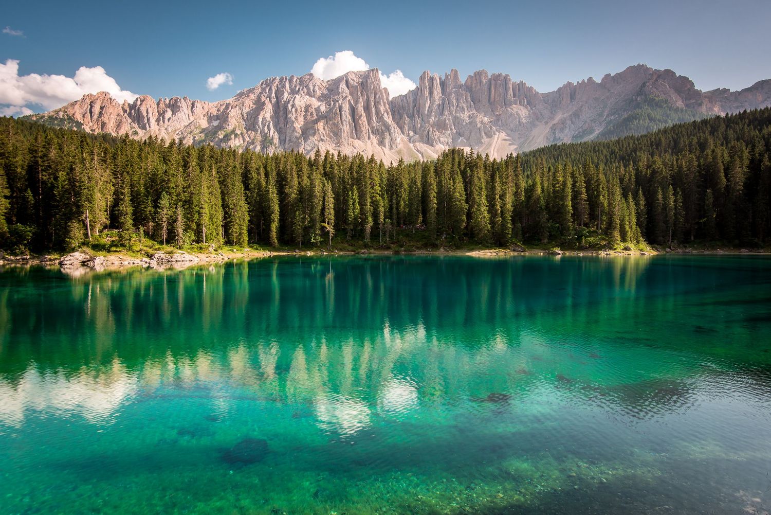 Le acque turchesi e cristalline del Lago di Carezza che riflettono la fitta foresta di abeti e il massiccio roccioso del Latemar.