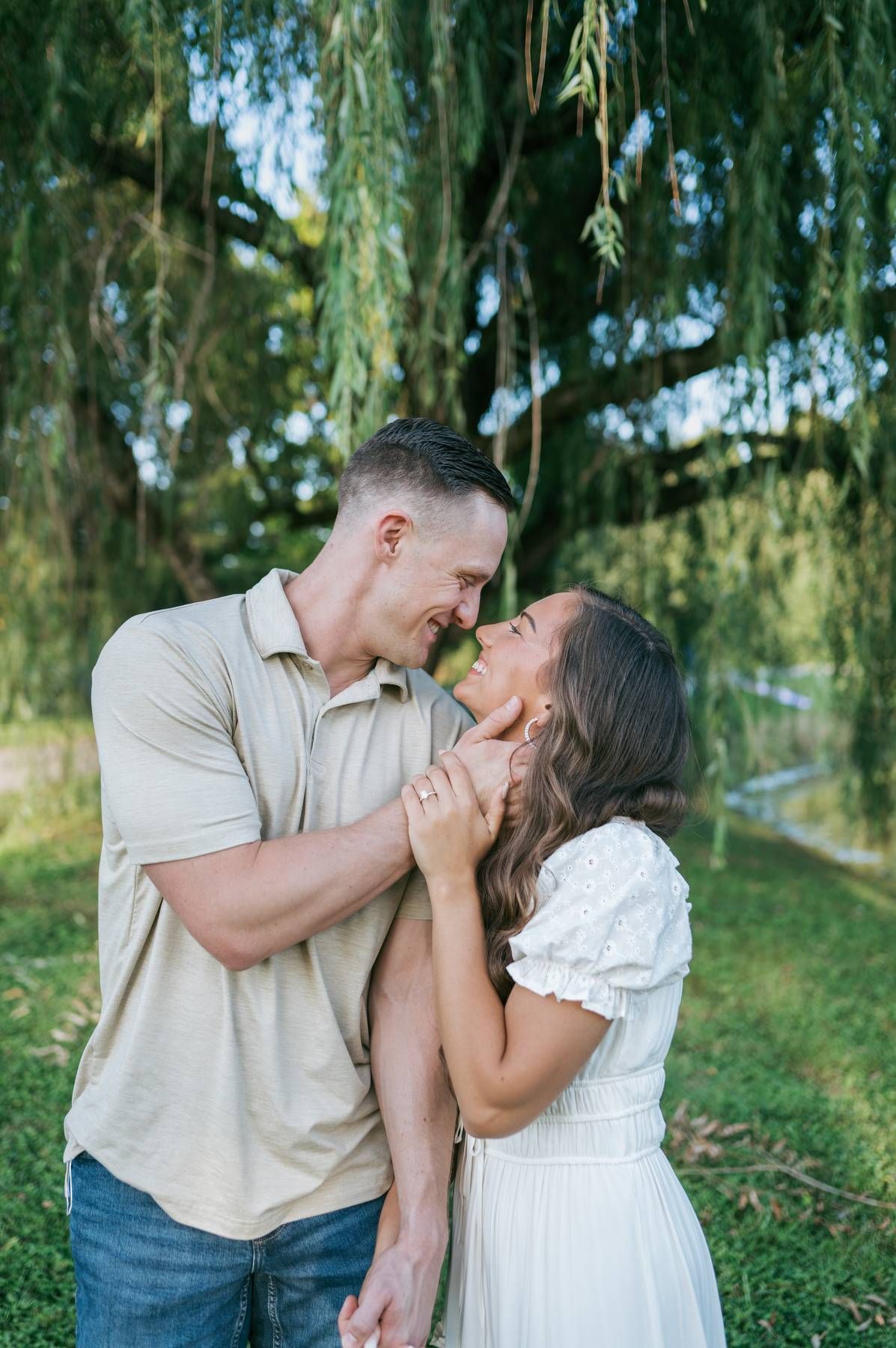 Happy couple almost kissing under weeping willow tree, man in tan polo and woman in white dress in North Carolina
