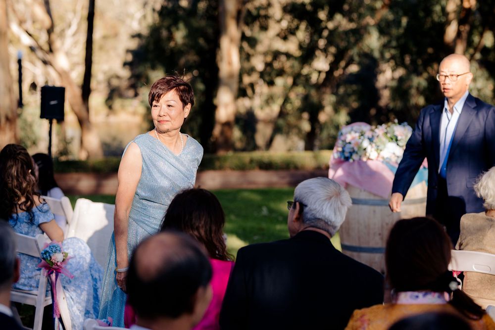 Couple walking down the aisle at an outdoor wedding ceremony surrounded by guests and lush green trees.