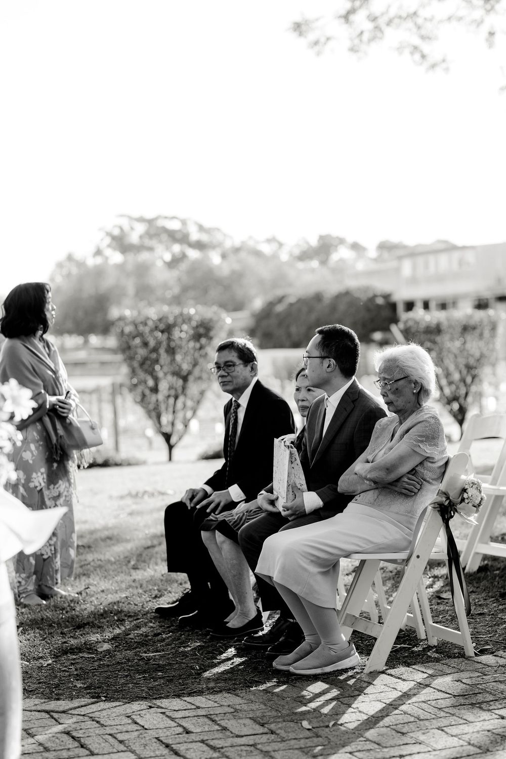 Black and white photo of wedding guests seated in white chairs during an outdoor ceremony.