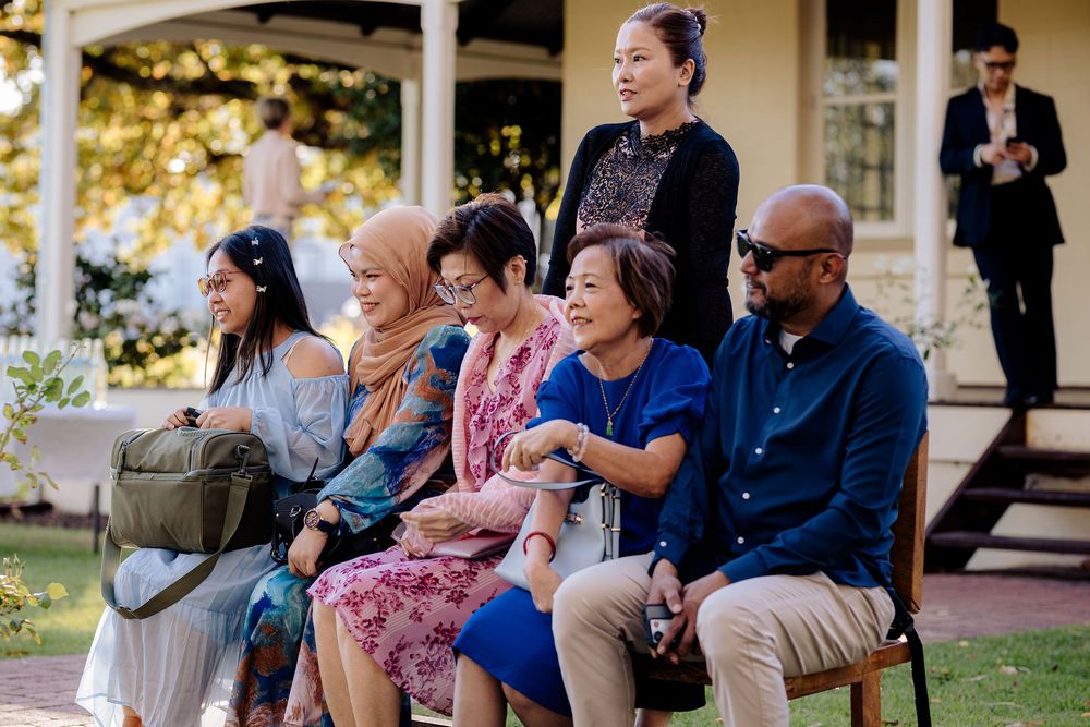 Diverse group of guests seated outdoors at a garden wedding ceremony, dressed in colorful formal attire.
