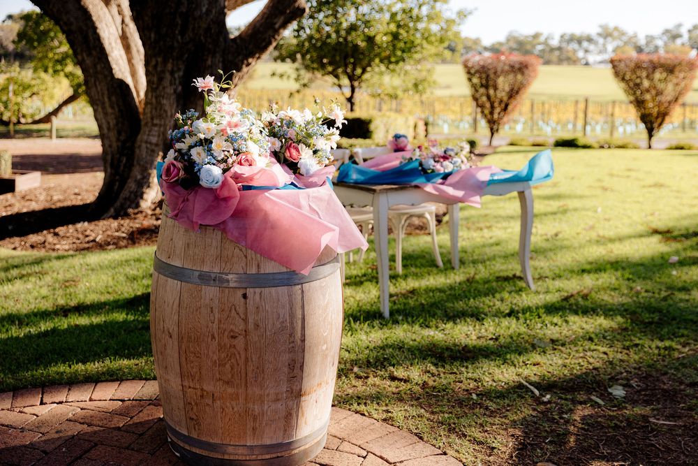Rustic wooden wine barrel decorated with flowers and pink tulle at an outdoor wedding reception with white chairs.