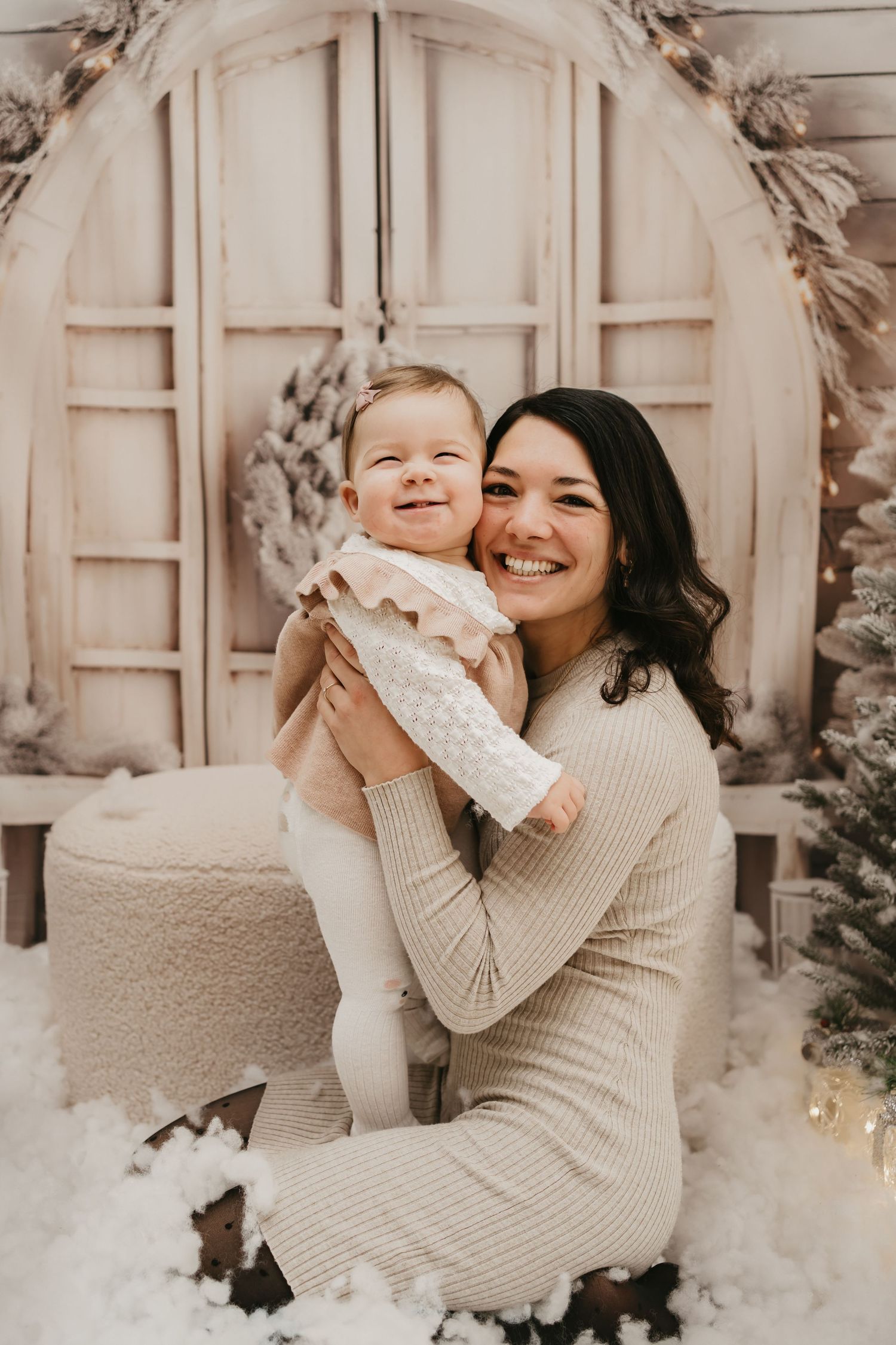 A joyful winter holiday scene with two people in cream sweaters sharing laughter amidst festive decorations and snow.