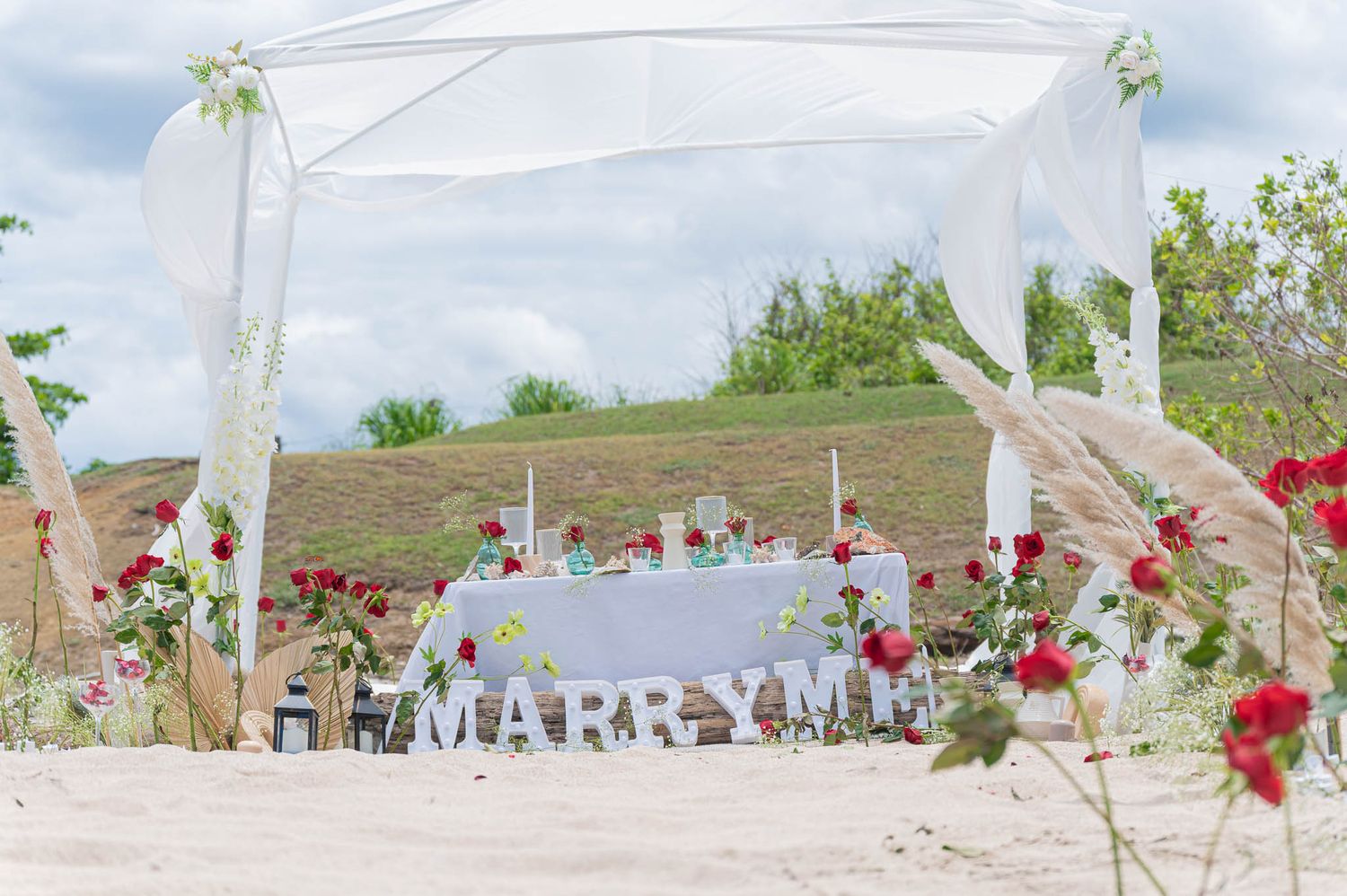 Romantic beach proposal setup with white canopy, red roses, and MARRY ME letters on sandy shore by chelo.photo