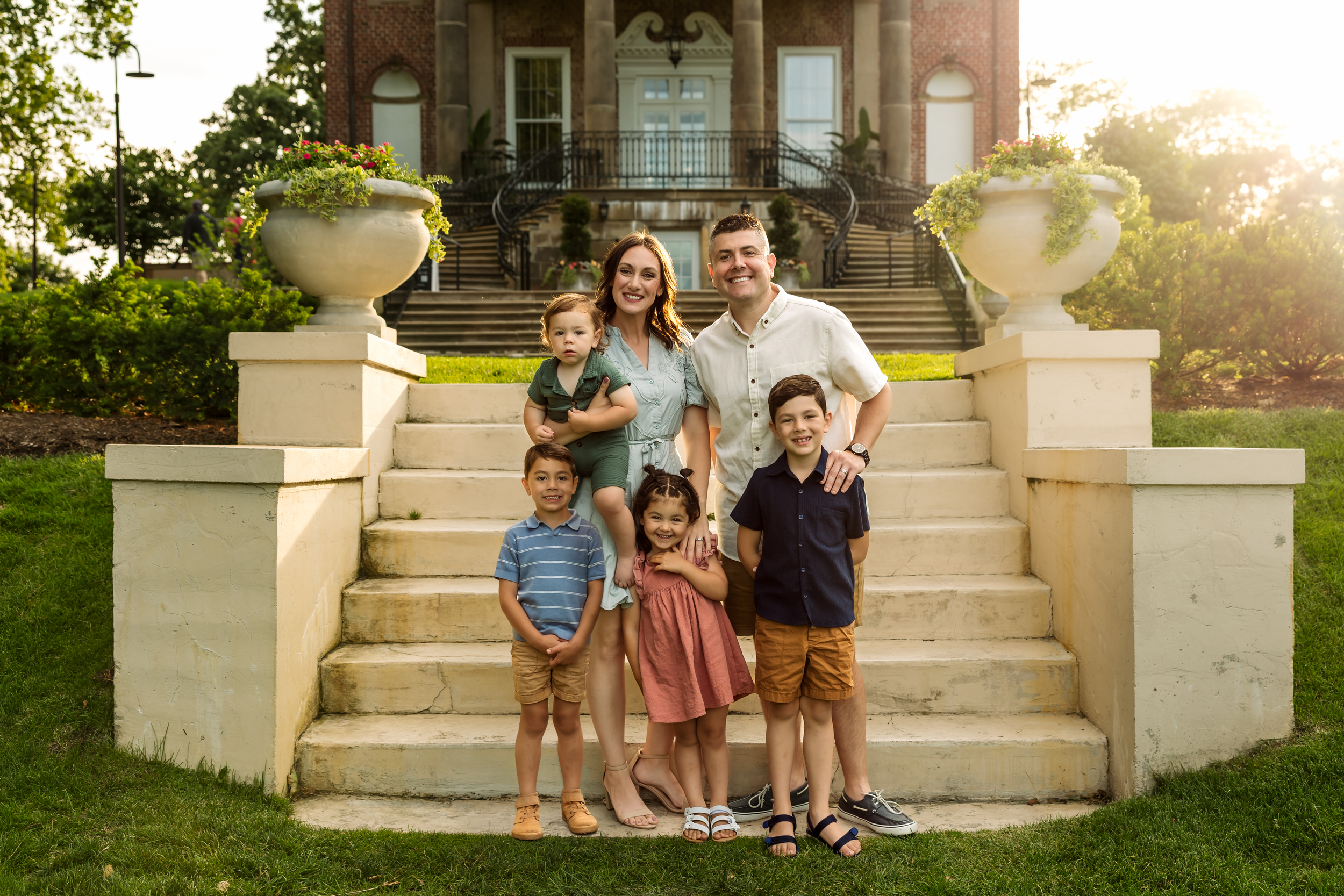 Family of six posing on stone steps outside a historic brick building during golden hour.