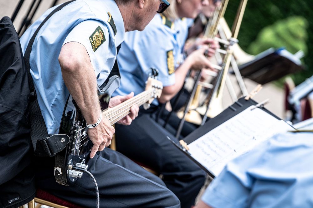 Police officers in uniform playing guitar and reading sheet music during an outdoor band performance.