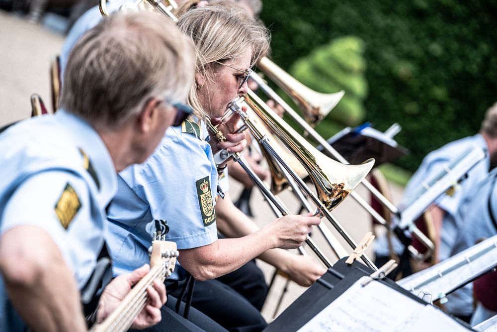 Musicians in blue uniforms playing trombone and guitar in an outdoor brass band performance.