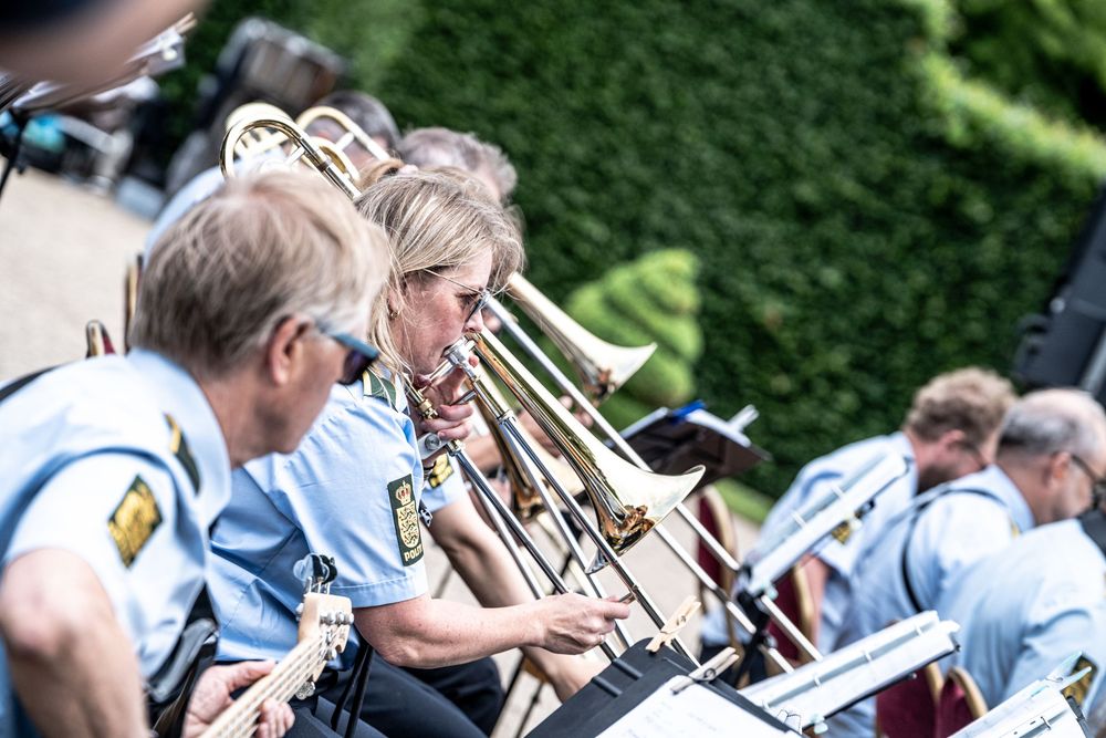 Brass band musicians in blue uniforms playing trombones outdoors at a summer concert.