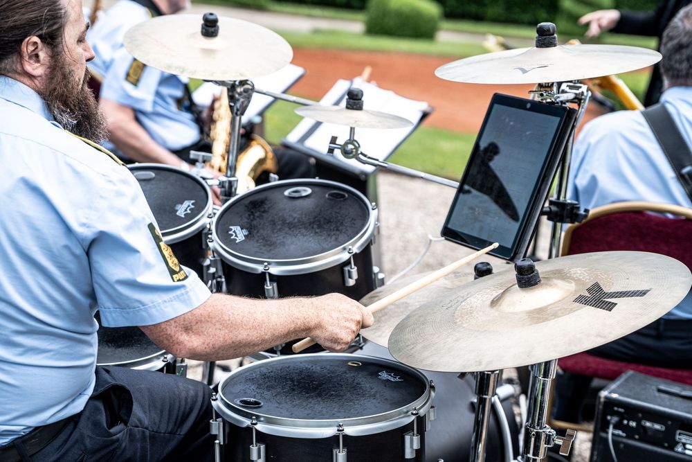 Musician in uniform playing drums with cymbals at an outdoor band performance.