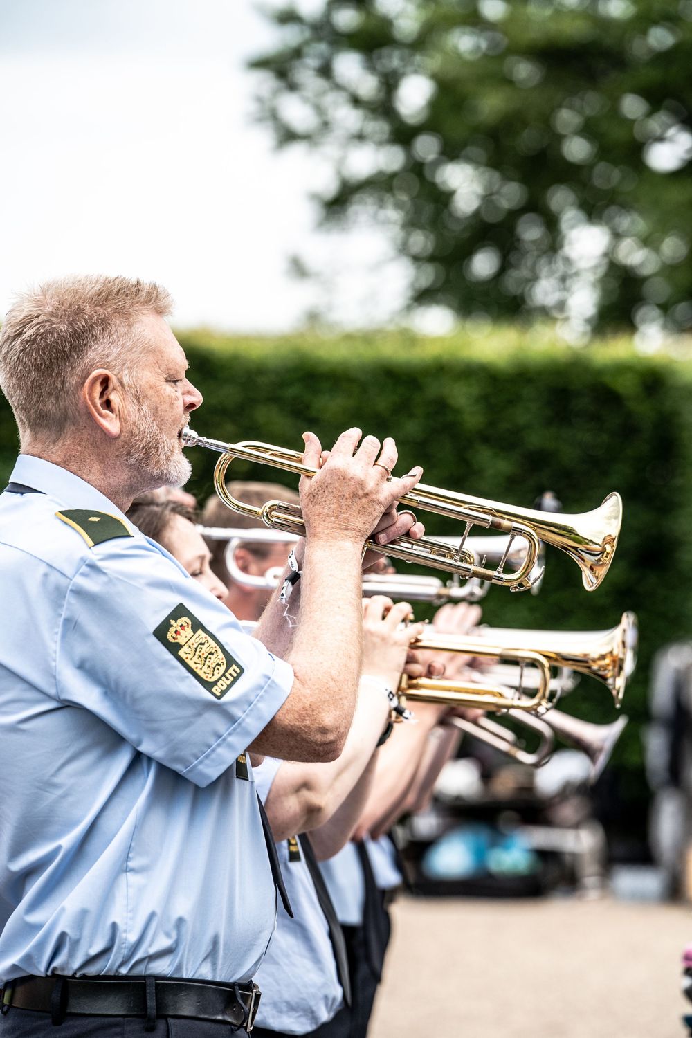 A uniformed police band musician plays trumpet outdoors at a public performance.