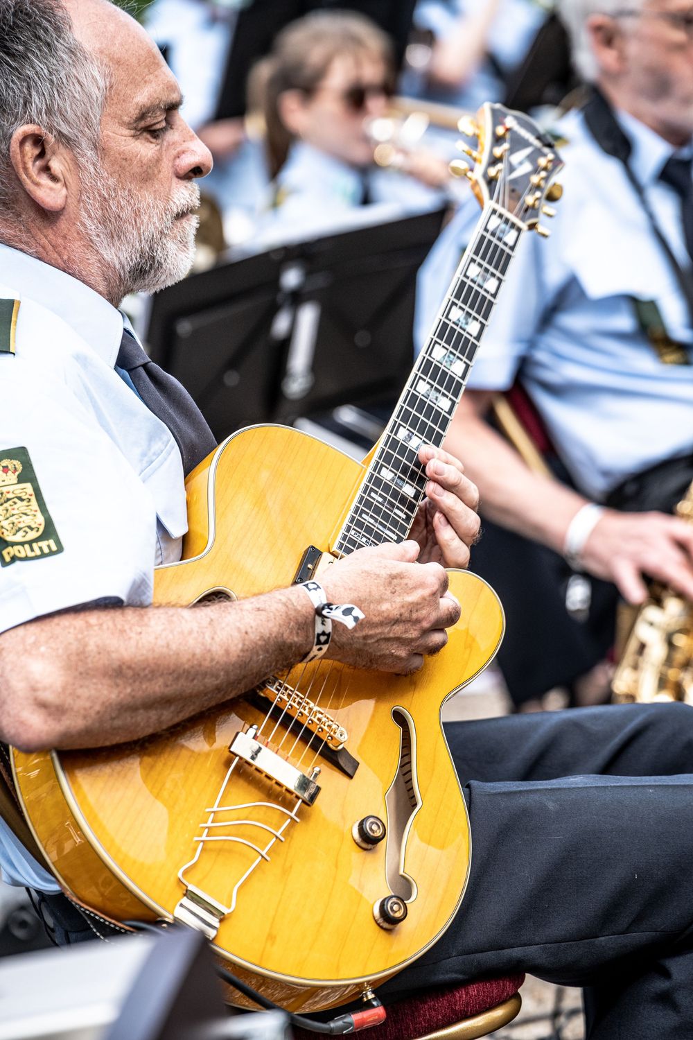Close-up of a police officer playing an archtop jazz guitar at an outdoor band concert.