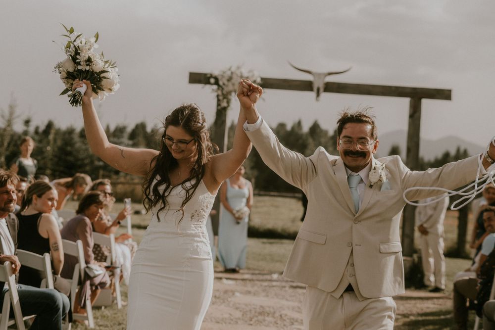 Joyful newlyweds celebrate walking down the aisle at an outdoor wedding ceremony, bride holding bouquet aloft.