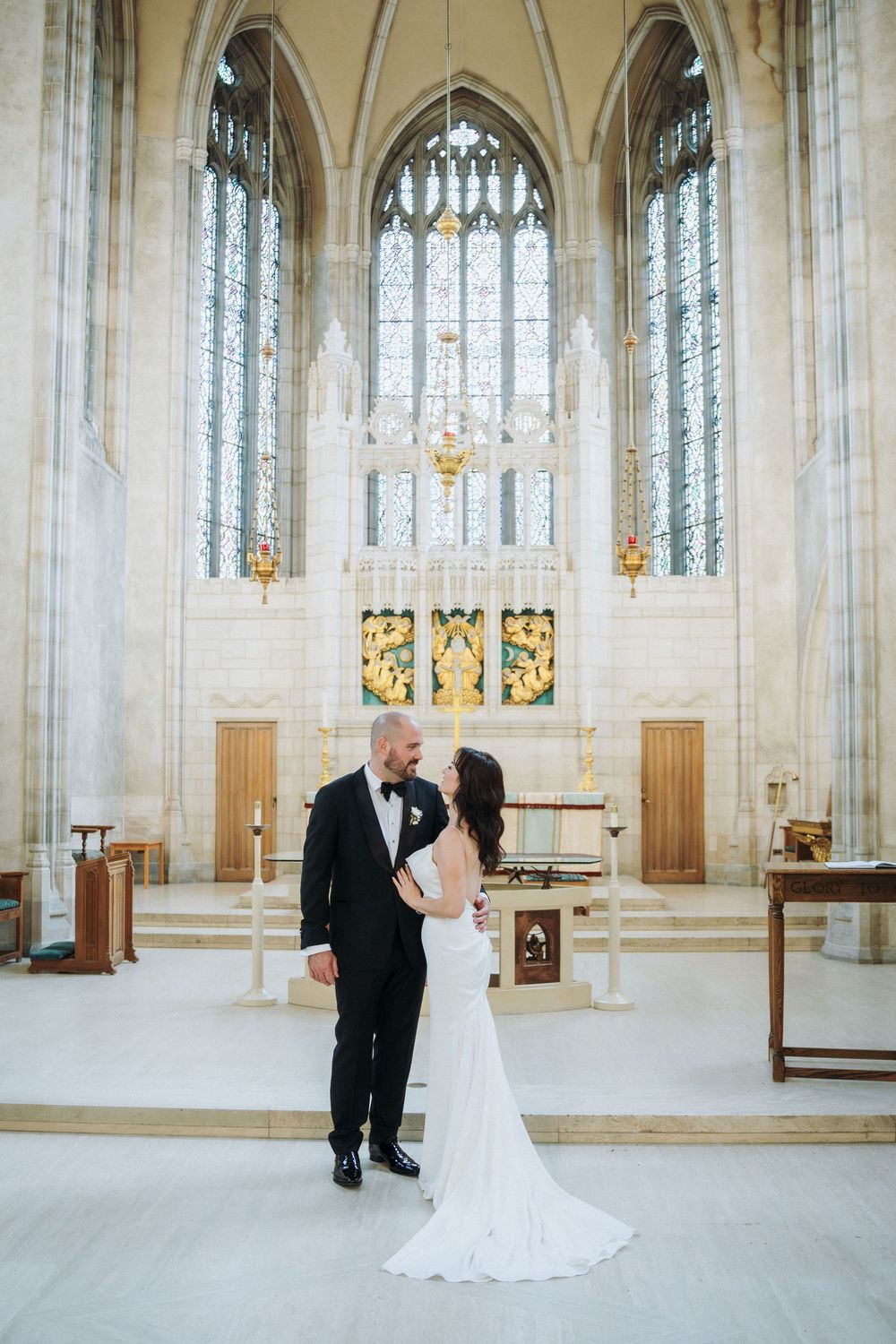 Bride and groom share a romantic moment at the altar of an elegant Gothic church with stained glass windows.