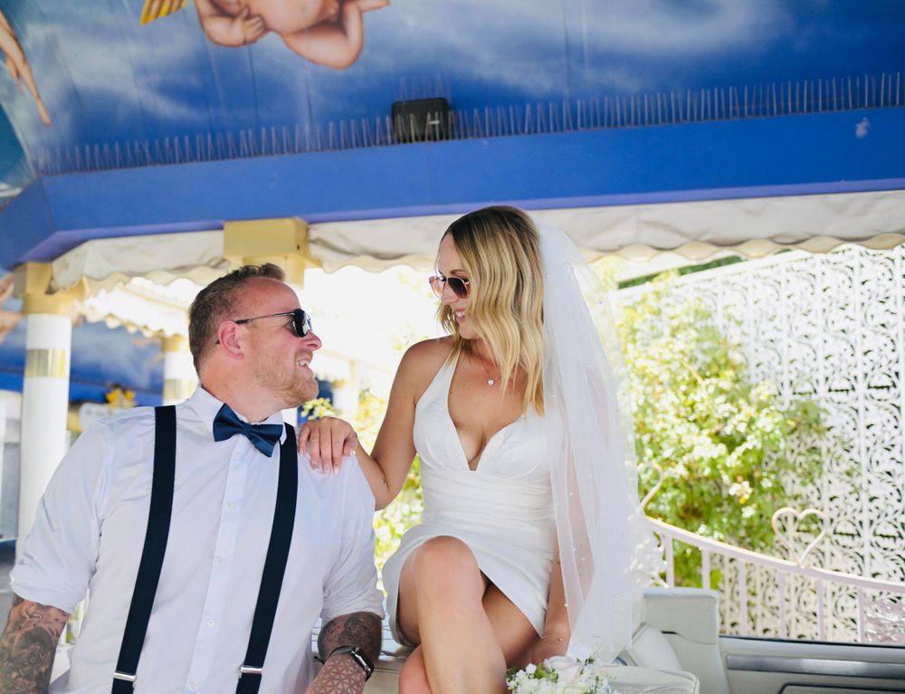 Bride sitting playfully with groom under a blue carousel canopy during Las Vegas wedding.