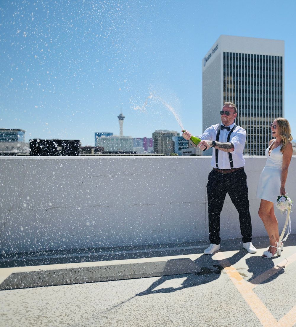 Couple celebrating wedding on Las Vegas rooftop, popping champagne with city skyline in background.