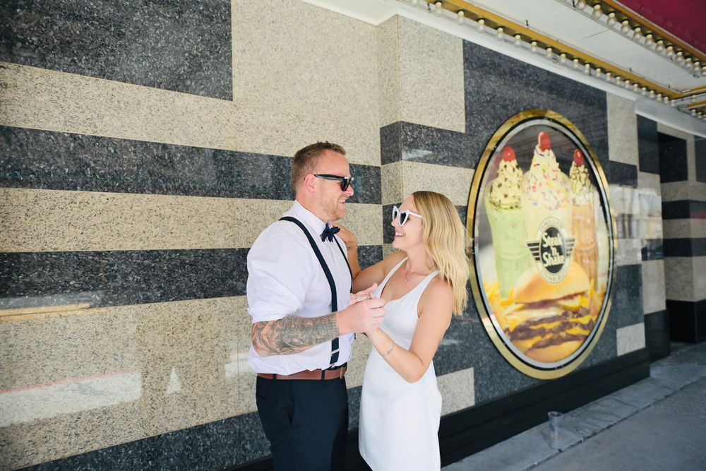 A couple in wedding attire shares a romantic moment outside a decorative building with a vintage mural in Las Vegas.