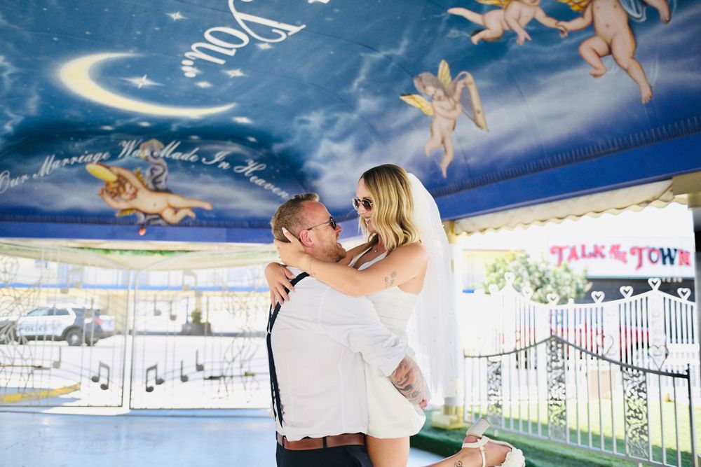 Bride and groom share romantic moment under painted angel ceiling mural at whimsical wedding venue.