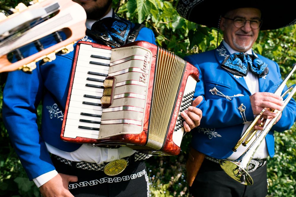Two musicians in blue traditional costumes playing accordion and trumpet outdoors.