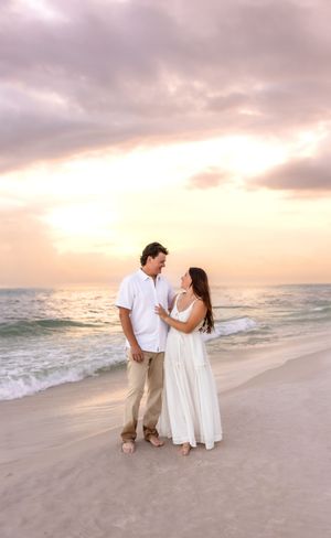 Couple gazing at each other on a beach at golden sunset, man in white shirt, woman in flowing white dress.