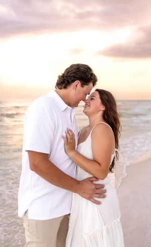 Happy couple in white outfits sharing a romantic moment on beach at golden sunset.