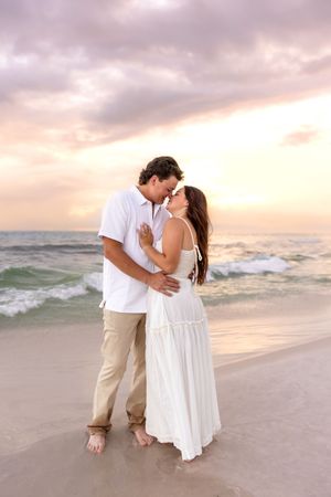 Romantic couple sharing a kiss on a sandy beach during a golden sunset by the ocean.