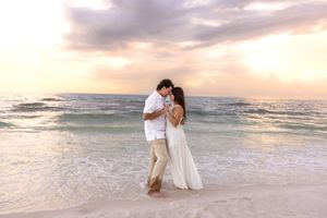 Romantic couple embracing on sandy beach at colorful sunset with turquoise ocean waves.