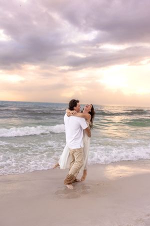 Man lifting woman in romantic embrace on beach at sunset.