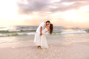Couple sharing a passionate dip kiss on beach with beautiful pink and orange sunset.