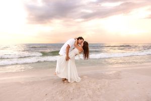 Couple sharing romantic dip kiss on sandy beach at vibrant sunset.