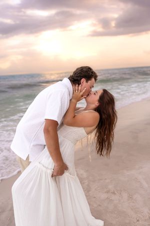 Romantic couple sharing a passionate kiss on a sandy beach during a beautiful pink and purple sunset.