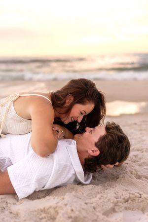 Happy couple laughing and playing together on sandy beach at sunset, sharing a joyful moment.